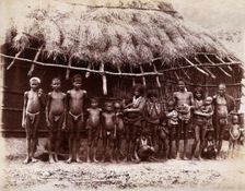 A group of adults and children standing in a line outside a bamboo hut with a thatched..., 1896/1897 Creator: Unknown