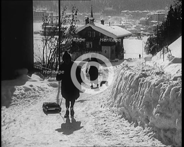A Group of Female Civilians Skiing down a Snowy Hill with a Picturesque Alpine Village..., 1920. Creator: British Pathe Ltd.