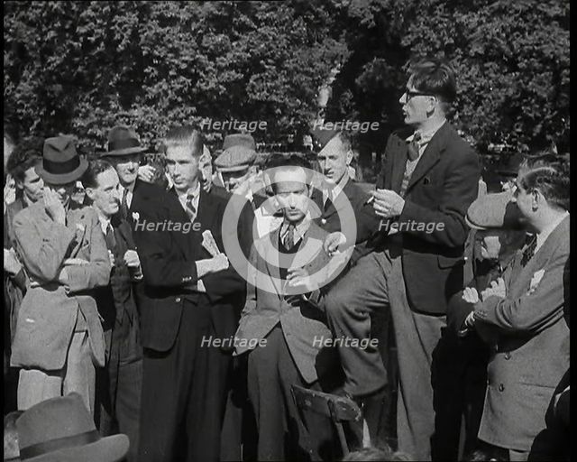 A Group of Male Civilians and One Soldier Listen to a Man With a Cigarette Standing on a..., 1938. Creator: British Pathe Ltd.