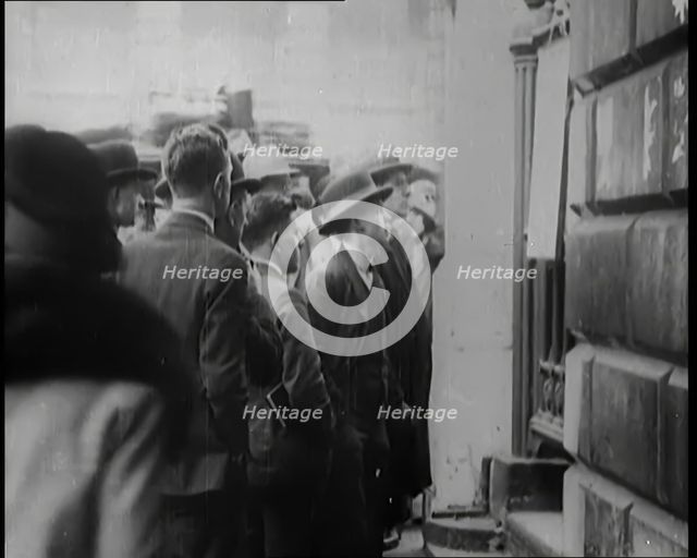 A Group of Male Civilians Looking at a Poster Attached to a Gate, 1926. Creator: British Pathe Ltd.