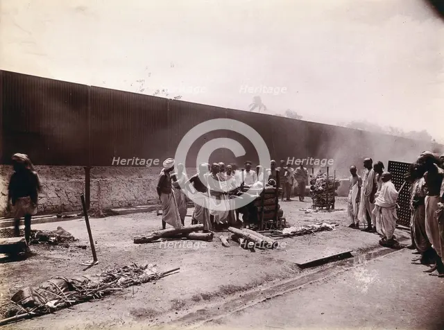 A group of men stand around the body of a man laid out on a pyre of logs during a Hindu...,  1896/97 Creator: Unknown.
