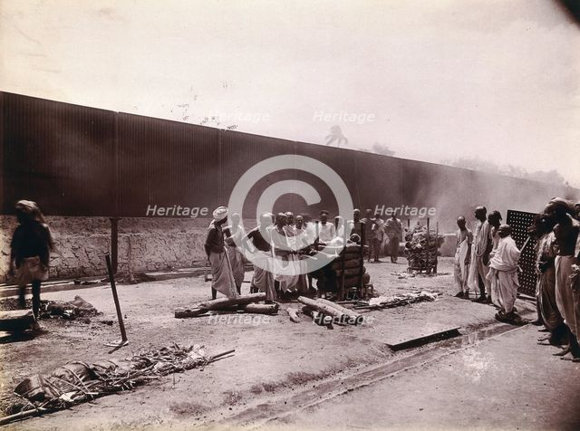 A group of men stand around the body of a man laid out on a pyre of logs during a Hindu...,  1896/97 Creator: Unknown.