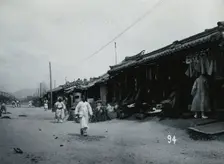 A line of shops beside a dusty street, with telegraph poles overhead, in Korea, c1900. Creator: Unknown