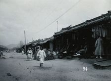 A line of shops beside a dusty street, with telegraph poles overhead, in Korea, c1900. Creator: Unknown