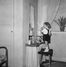 A little girl uses her mother's lipstick in front of a mirror, Sweden