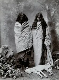 A man and woman of the Toda tribe standing in a photographic studio, with a dog lying..., c1900. Creator: Unknown