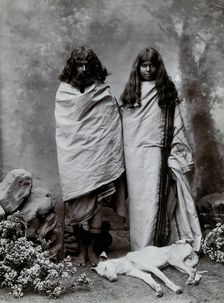 A man and woman of the Toda tribe standing in a photographic studio, with a dog lying..., c1900. Creator: Unknown