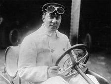 A man at the wheel of his car dressed in a driving coat and goggles