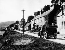 A man by his car in a village lane, 1900