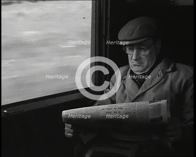 A Man in a Flat Cap and Spectacles Reading a Folded Newspaper in the Window Seat of a Train..., 1938 Creator: British Pathe Ltd.