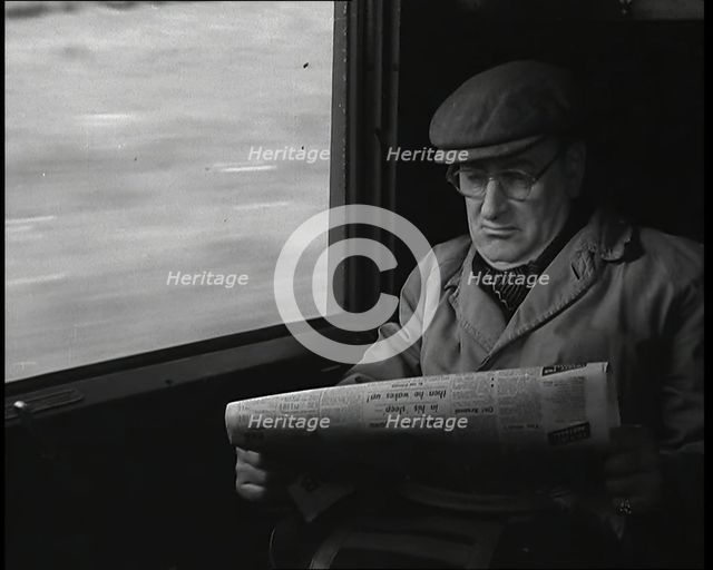 A Man in a Flat Cap and Spectacles Reading a Folded Newspaper in the Window Seat of a Train..., 1938 Creator: British Pathe Ltd.