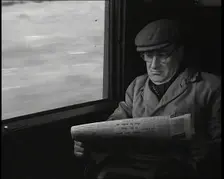 A Man in a Flat Cap and Spectacles Reading a Folded Newspaper in the Window Seat of a Train..., 1938 Creator: British Pathe Ltd