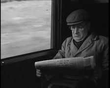 A Man in a Flat Cap and Spectacles Reading a Folded Newspaper in the Window Seat of a Train..., 1938 Creator: British Pathe Ltd