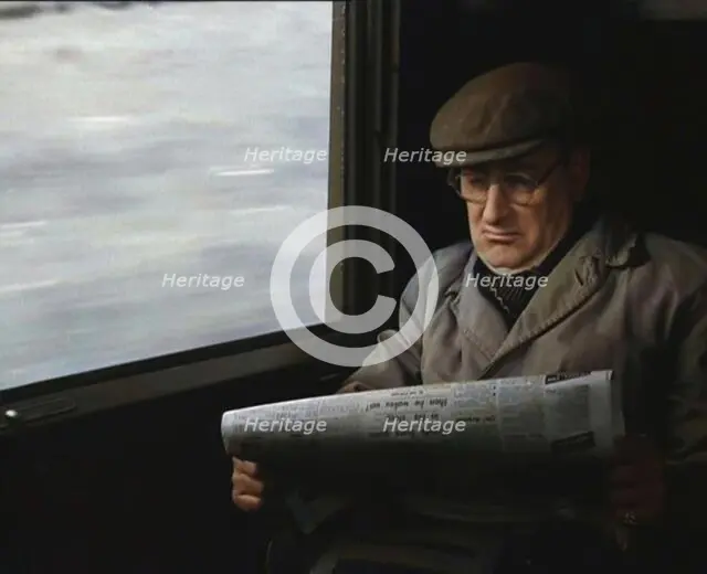 A Man in a Flat Cap and Spectacles Reading a Folded Newspaper in the Window Seat of a Train..., 1938 Creator: British Pathe Ltd.