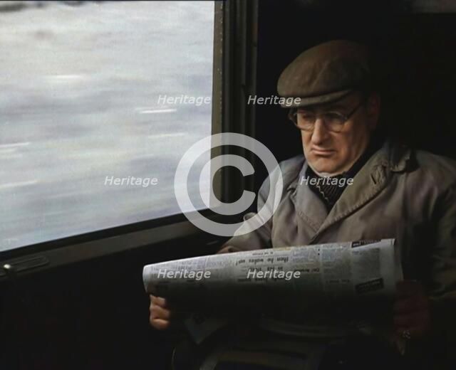 A Man in a Flat Cap and Spectacles Reading a Folded Newspaper in the Window Seat of a Train..., 1938 Creator: British Pathe Ltd.