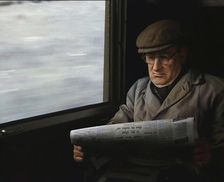 A Man in a Flat Cap and Spectacles Reading a Folded Newspaper in the Window Seat of a Train..., 1938 Creator: British Pathe Ltd