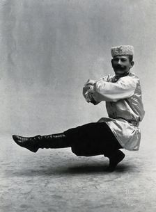 A man, in a satin tunic and fur hat, dancing a "Cossack" measure in a studio setting, 1899-1908. Creator: Unknown