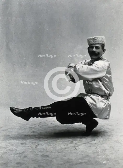 A man, in a satin tunic and fur hat, dancing a "Cossack" measure in a studio setting, 1899-1908. Creator: Unknown.