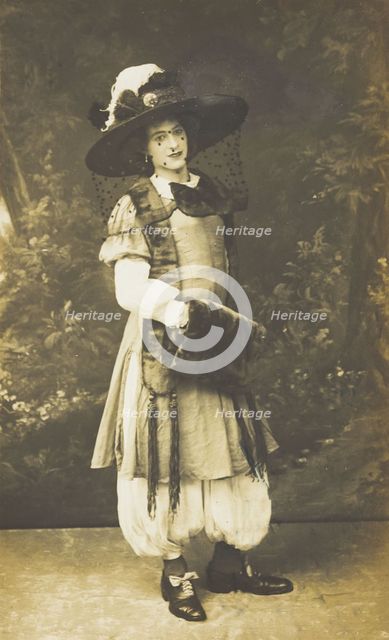 A man in drag wearing a very large hat with a veil, stands in front of a painted..., 1911. Creator: Unknown.