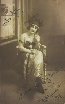 A man in drag (Charlie) sits face-on, wearing detailed costume, with a window painted..., 1919. Creator: Unknown