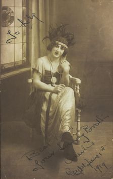 A man in drag (Charlie) sits face-on, wearing detailed costume, with a window painted..., 1919. Creator: Unknown