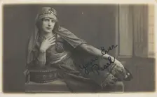 A man in drag, poses wearing delicate attire; curled up on a piece of furniture, [1910-1919?]. Creator: Unknown
