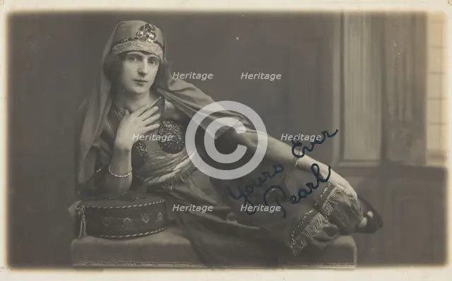 A man in drag, poses wearing delicate attire; curled up on a piece of furniture, [1910-1919?]. Creator: Unknown.