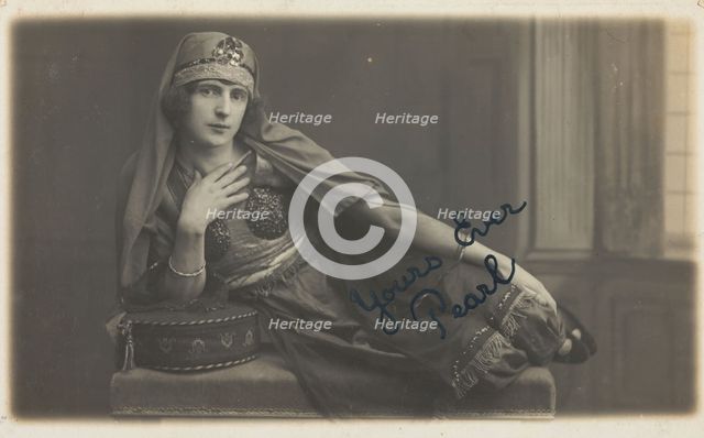 A man in drag, poses wearing delicate attire; curled up on a piece of furniture, [1910-1919?]. Creator: Unknown.