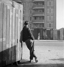 A man leaning on a street corner hoarding, possibly Rugmere on Ferdinand St, Camden, 1945-50. Creator: John Gay