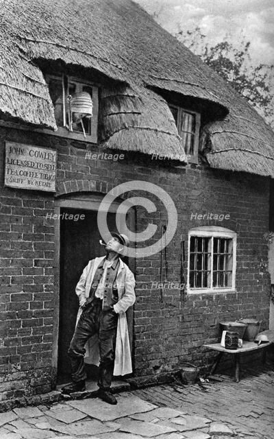 A man smoking a pipe outside a shop, Worcestershire, c1922.Artist: AW Cutler