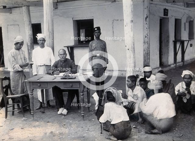 A man sitting at a table examining passports, during a plague epidemic in Mandalay, 1906. Creator: Unknown.