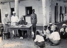 A man sitting at a table examining passports, during a plague epidemic in Mandalay, 1906. Creator: Unknown