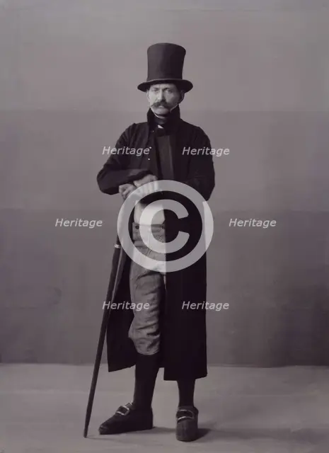 A man poses in folk costume with a long coat and a top hat, 1880-1907. Creator: Helene Edlund.