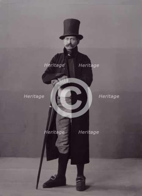 A man poses in folk costume with a long coat and a top hat, 1880-1907. Creator: Helene Edlund.