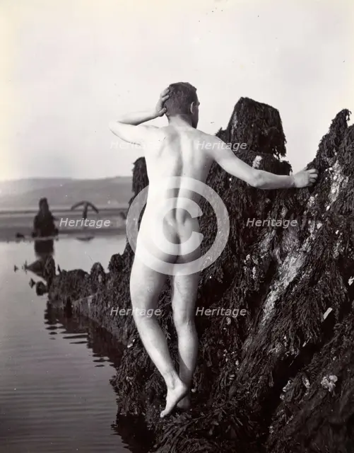 A man posing naked, with his back to the camera, standing on a rocky outcrop, c1900. Creator: Unknown.