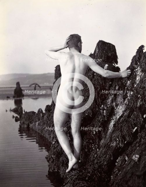 A man posing naked, with his back to the camera, standing on a rocky outcrop, c1900. Creator: Unknown.