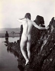A man posing naked, with his back to the camera, standing on a rocky outcrop, c1900. Creator: Unknown