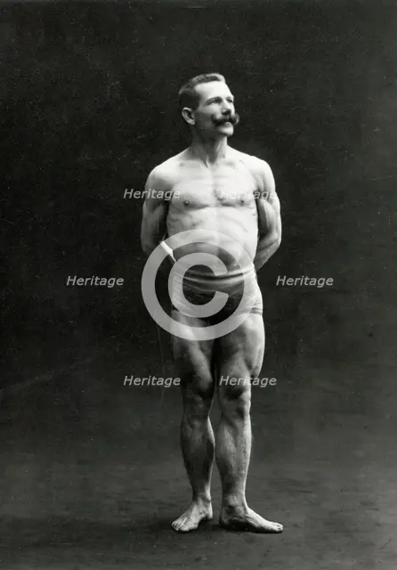 A male bodybuilder wearing bathing trunks, posing in a studio setting, between 1899 and 1908. Creator: Unknown.