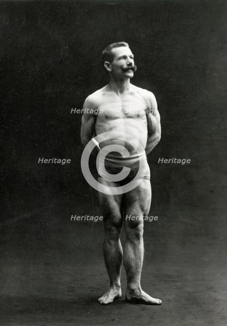 A male bodybuilder wearing bathing trunks, posing in a studio setting, between 1899 and 1908. Creator: Unknown.
