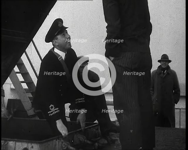 A Male Customs Official Standing by a Hatch and Talking to a Man on Board a Large Ship in..., 1939. Creator: British Pathe Ltd.