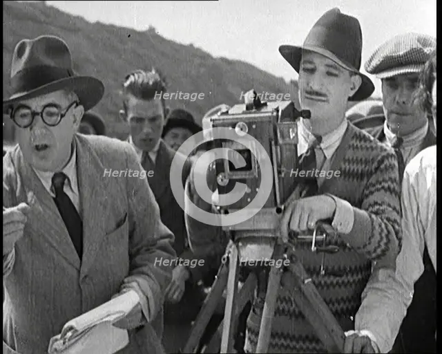 A Male Cameraman Cranking a Camera On a Film Set as the Male Director Instructs Actors, 1920s. Creator: British Pathe Ltd.
