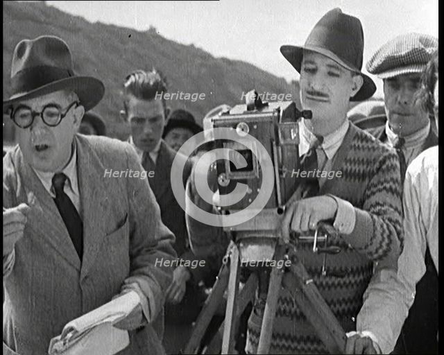 A Male Cameraman Cranking a Camera On a Film Set as the Male Director Instructs Actors, 1920s. Creator: British Pathe Ltd.