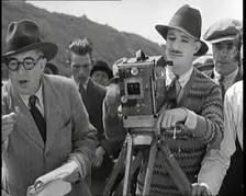 A Male Cameraman Cranking a Camera On a Film Set as the Male Director Instructs Actors, 1920s. Creator: British Pathe Ltd
