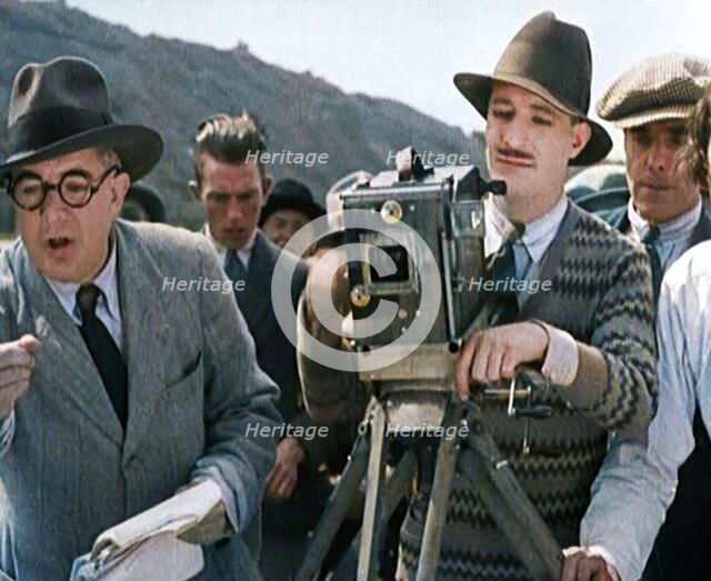 A Male Cameraman Cranking a Camera On a Film Set as the Male Director Instructs Actors, 1920s. Creator: British Pathe Ltd.