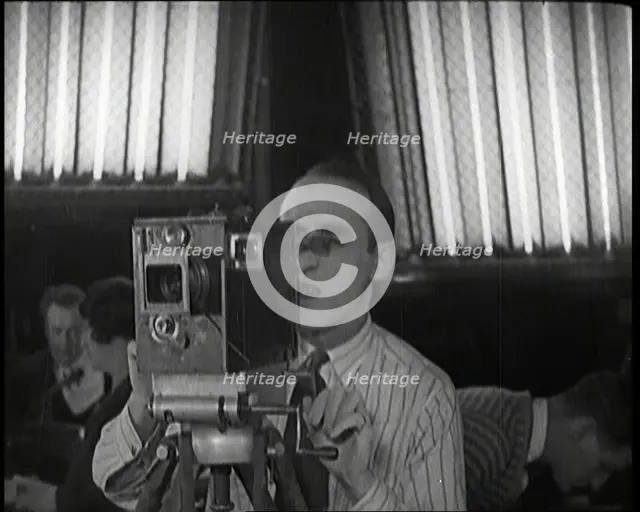 A Male Cameraman Films a Scene Whilst Lights Illuminate Behind Him, 1920s. Creator: British Pathe Ltd.
