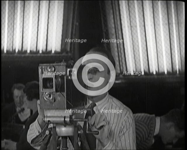 A Male Cameraman Films a Scene Whilst Lights Illuminate Behind Him, 1920s. Creator: British Pathe Ltd.