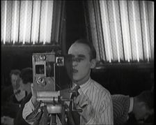 A Male Cameraman Films a Scene Whilst Lights Illuminate Behind Him, 1920s. Creator: British Pathe Ltd