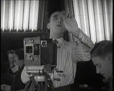 A Male Cameraman Films a Scene Whilst Lights Illuminate Behind Him, 1920s. Creator: British Pathe Ltd