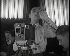 A Male Cameraman Films a Scene Whilst Lights Illuminate Behind Him, 1920s. Creator: British Pathe Ltd