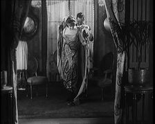 A Male Civilian Helping a Female Civilian Remove Her Fur Coat Revealing an Ornated Gown, 1920. Creator: British Pathe Ltd